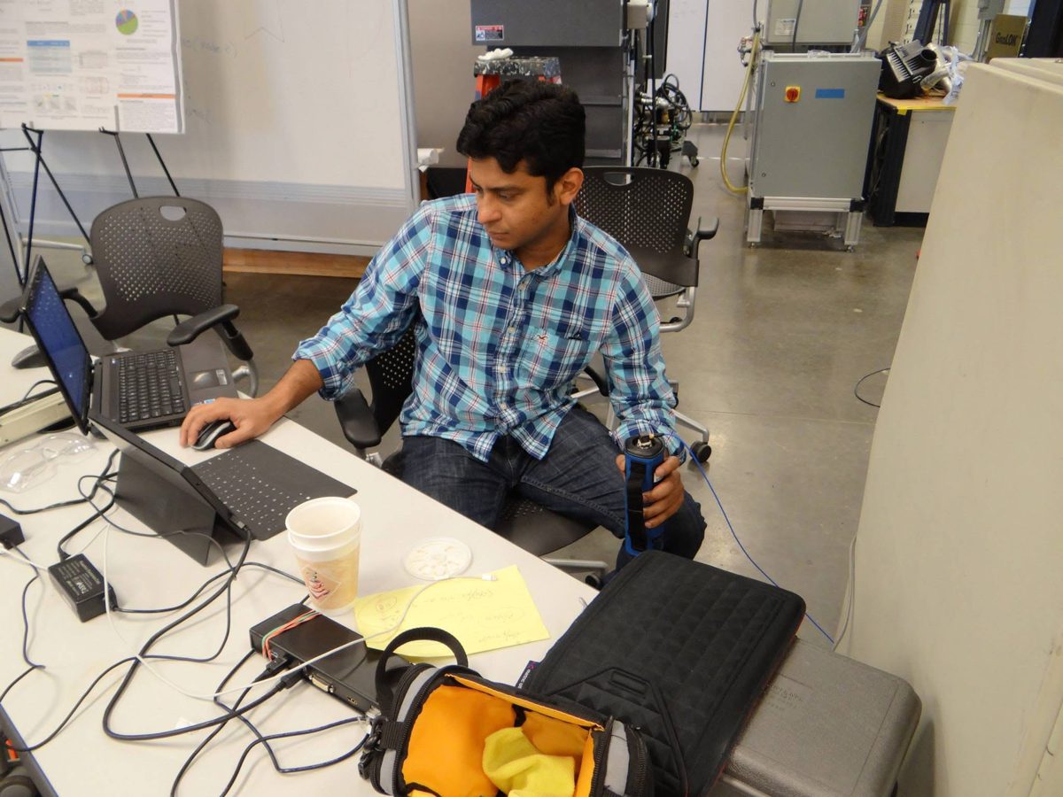 Hasan Pasha at a laptop test station in a vehicle test lab, cables and data acquisition hardware on the bench.